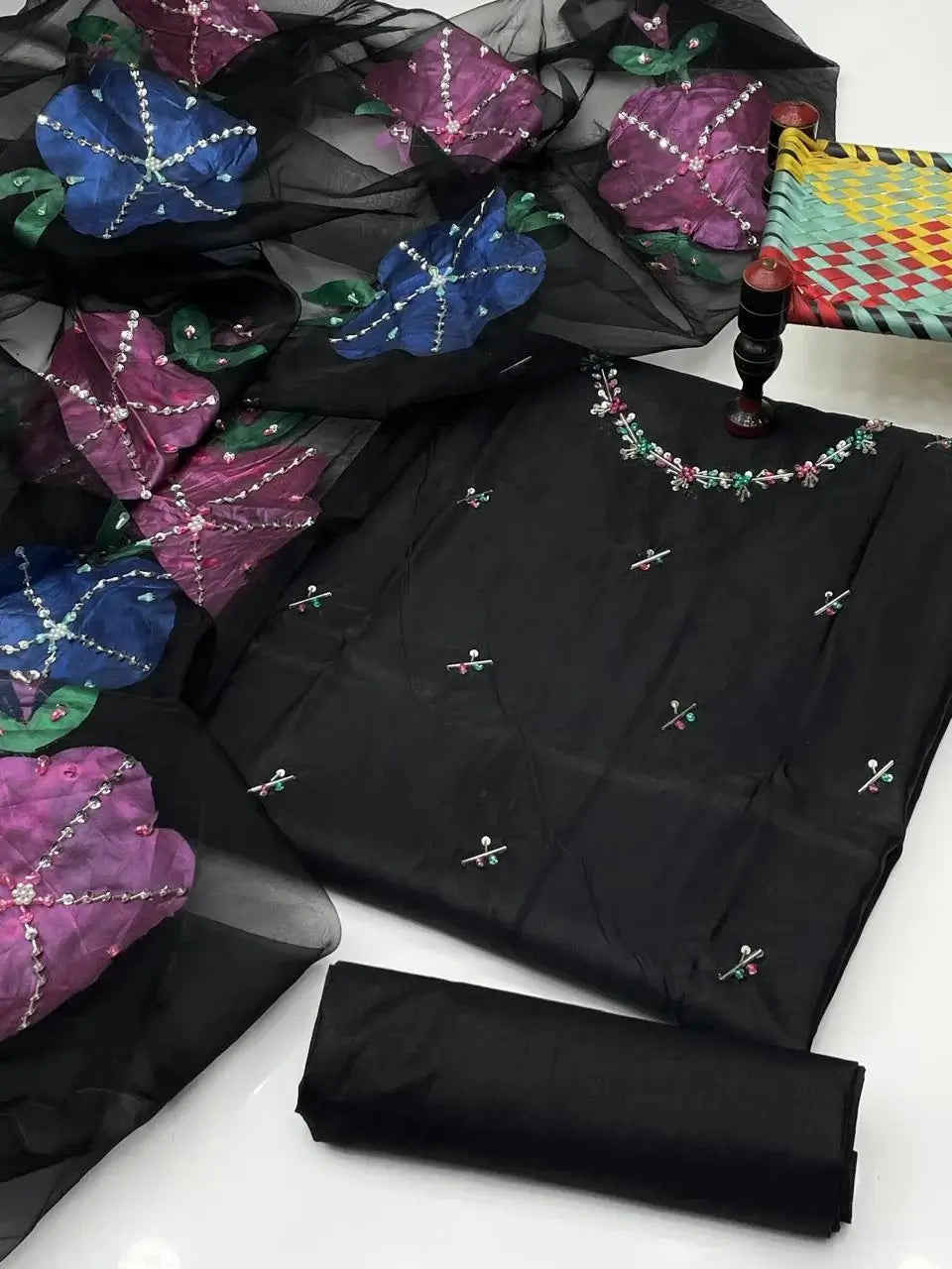 Elegant black unstitched dress set with colorful floral embroidery and accompanying fabric roll.