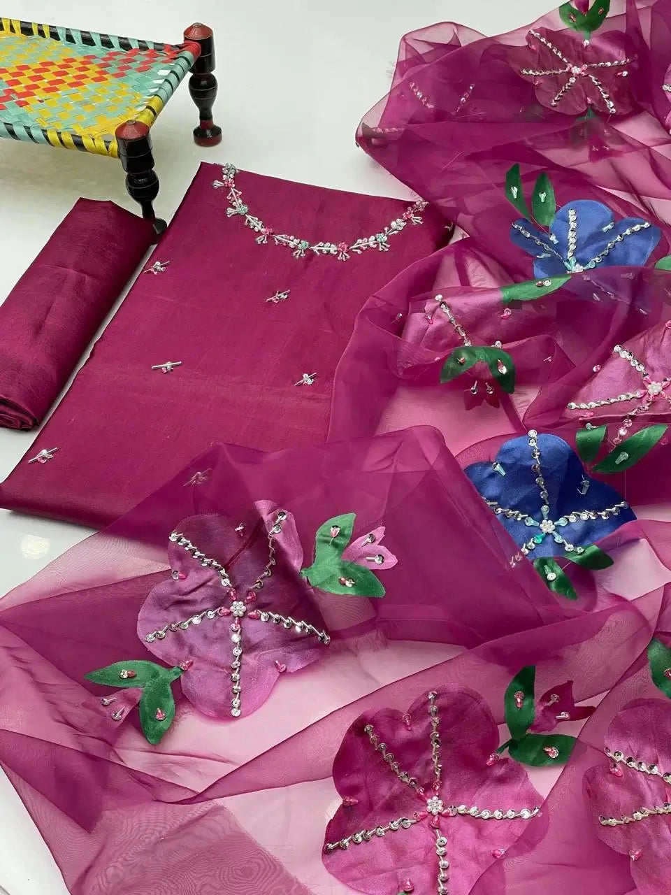 Elegant unstitched wedding dress set with floral embroidery in vibrant pink, green, and blue hues, beautifully arranged.